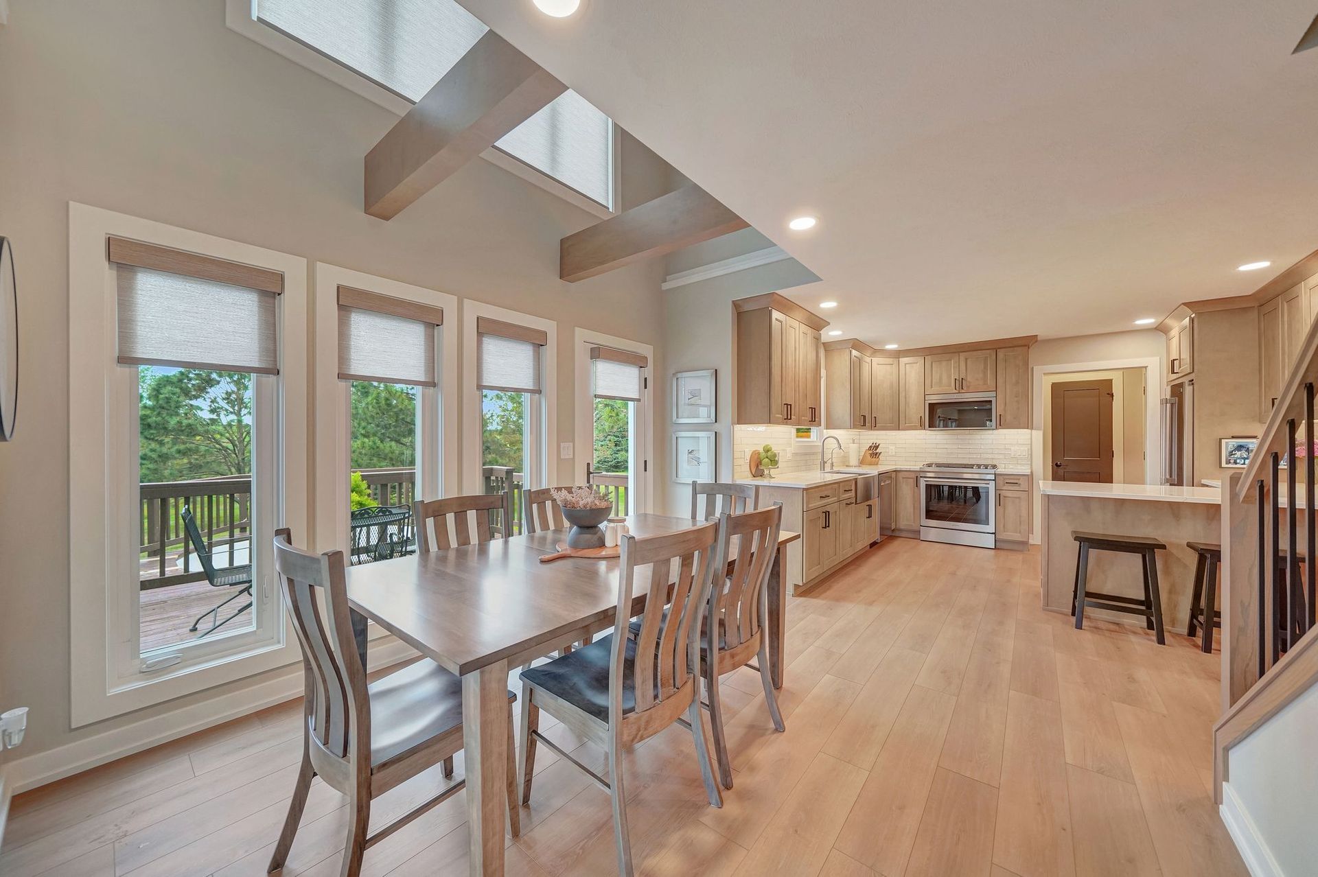 Dining room with a table and chairs, adjacent to a kitchen with light-colored cabinets, windows, and skylights.
