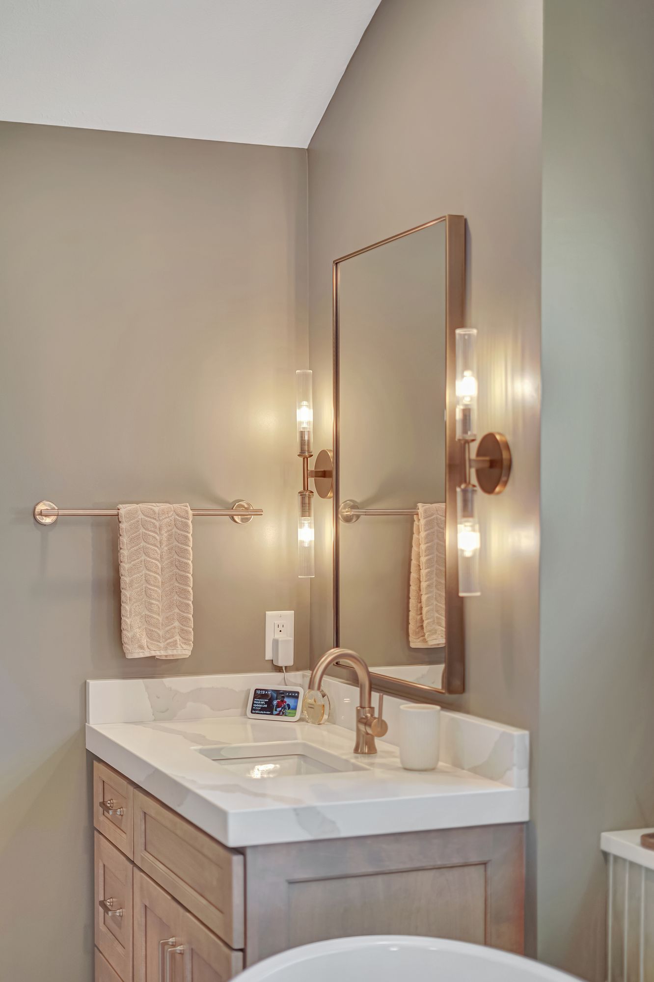 Bathroom vanity with a mirror, sconces, and towel rack. Tan and white color scheme.