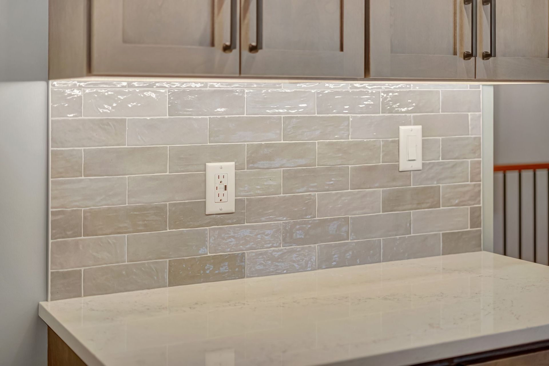 Kitchen backsplash with light beige brick-style tiles, outlets, and cabinets above a countertop.