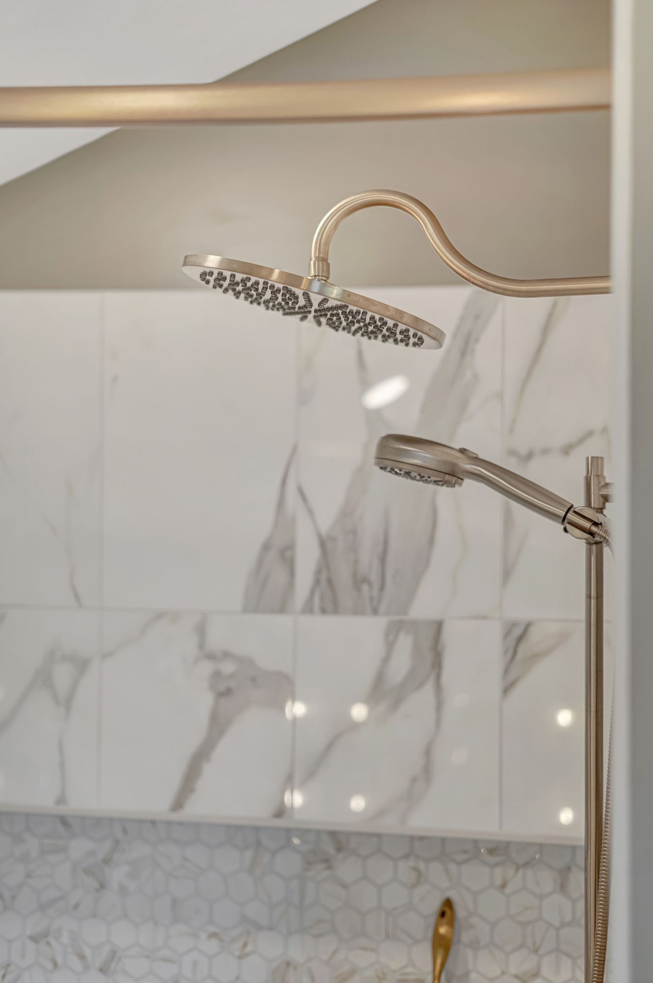 Shower with two showerheads, one overhead and one handheld, against marble tile.
