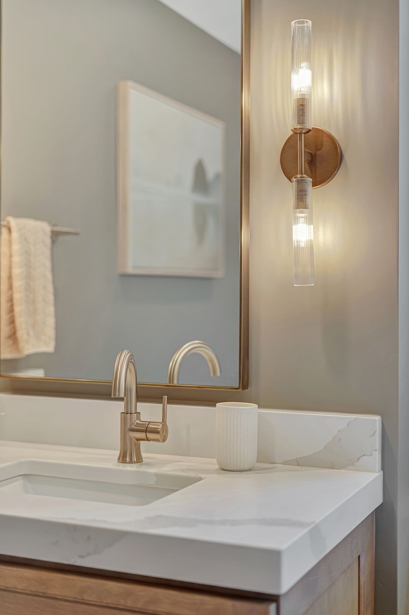 Bathroom vanity with gold-toned fixtures, a mirror, and a two-bulb wall sconce.