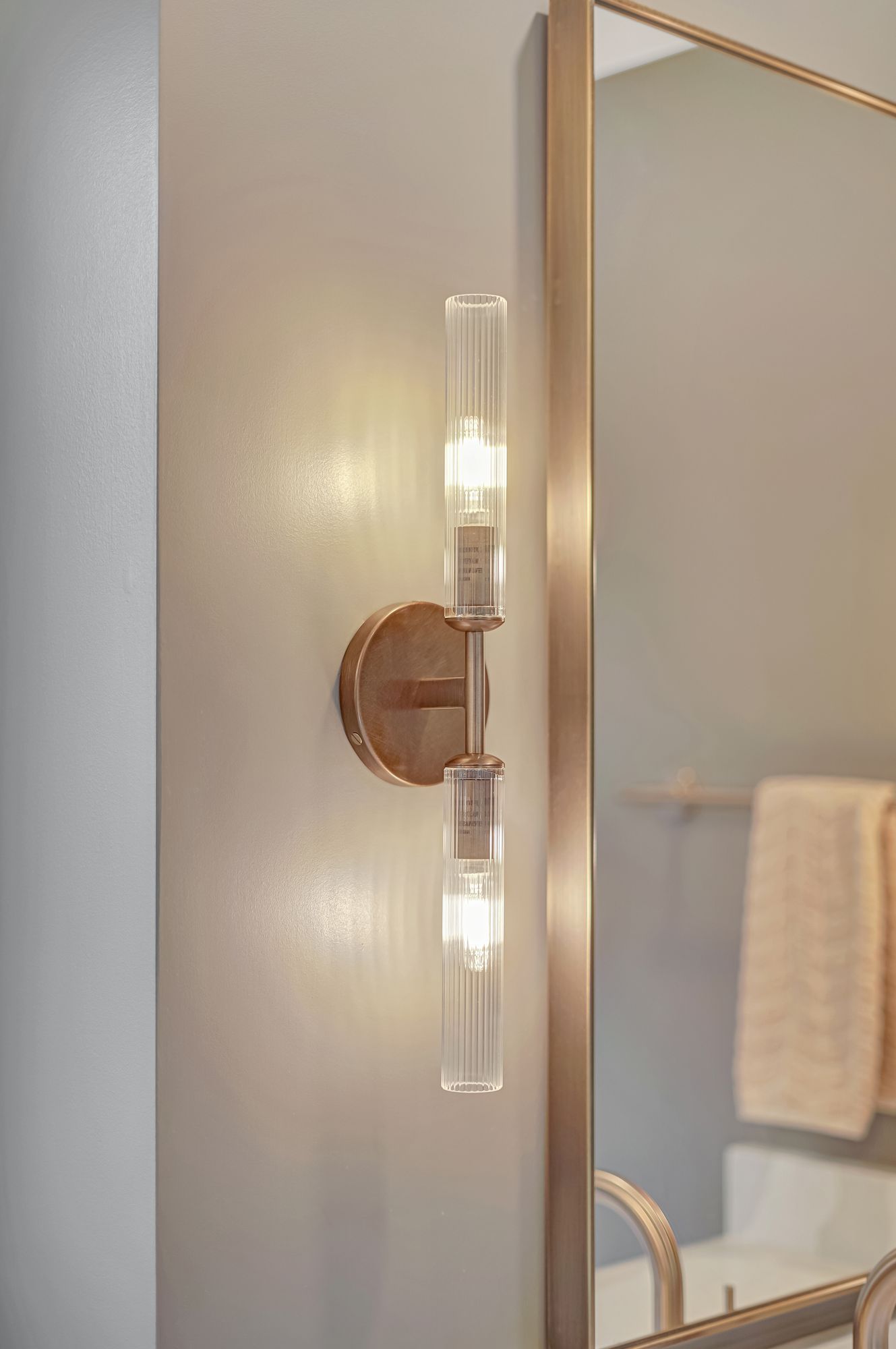 Brass vanity light fixture with two glass cylinder shades next to a mirror in a bathroom.