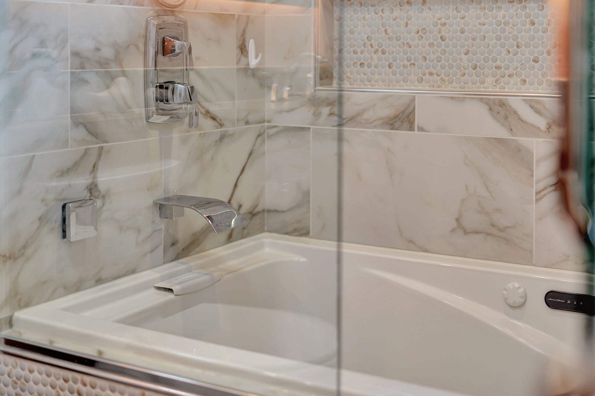 A bathtub in a bathroom with marble tiles and a glass shower door.