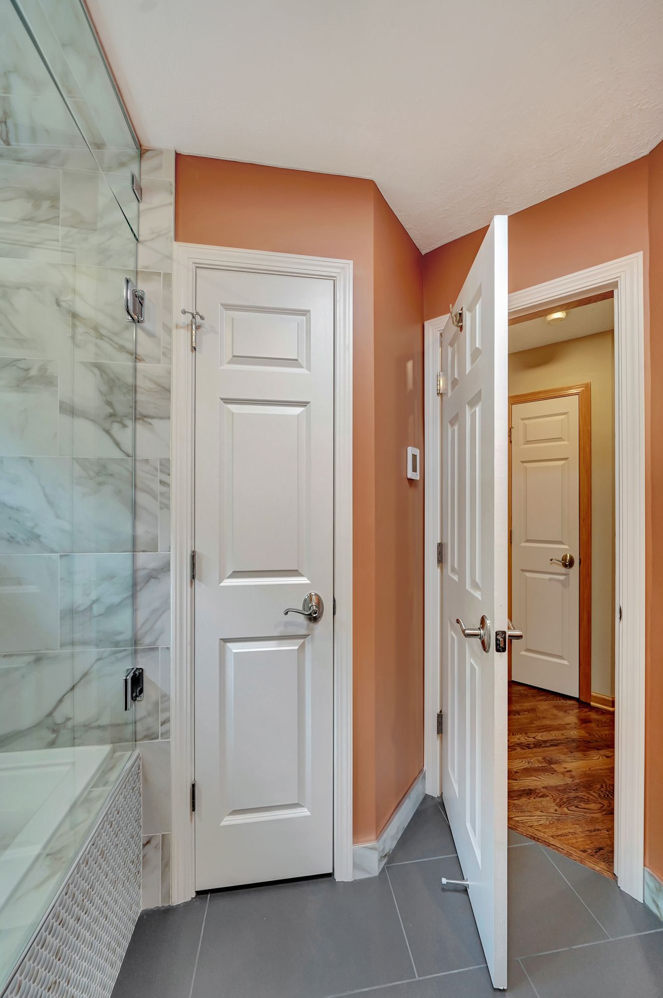 A bathroom with a walk in shower and two doors open.