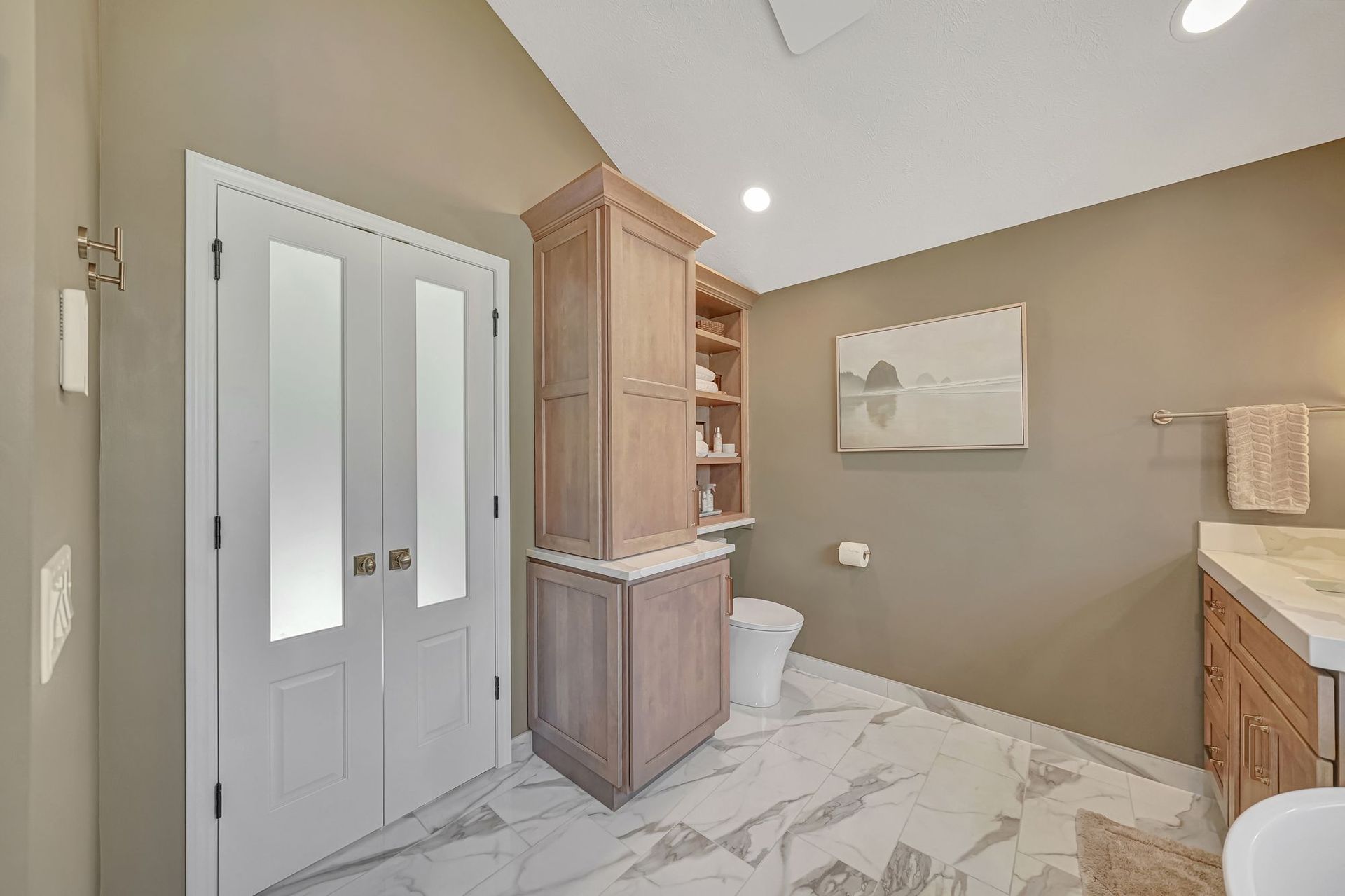 Bathroom with tall cabinet, double doors, beige walls, and white marble-look floor.