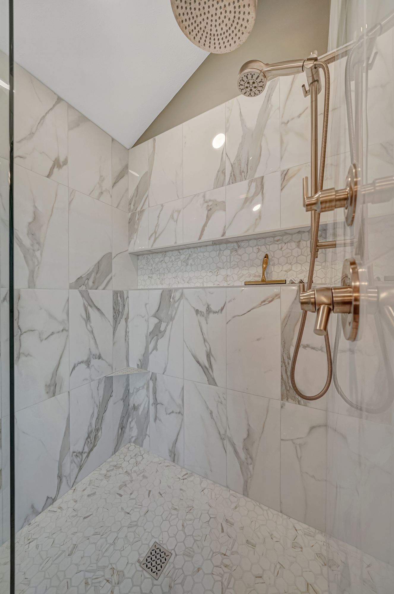 Marble-tiled shower with gold fixtures; includes a bench, shelf, and two showerheads.
