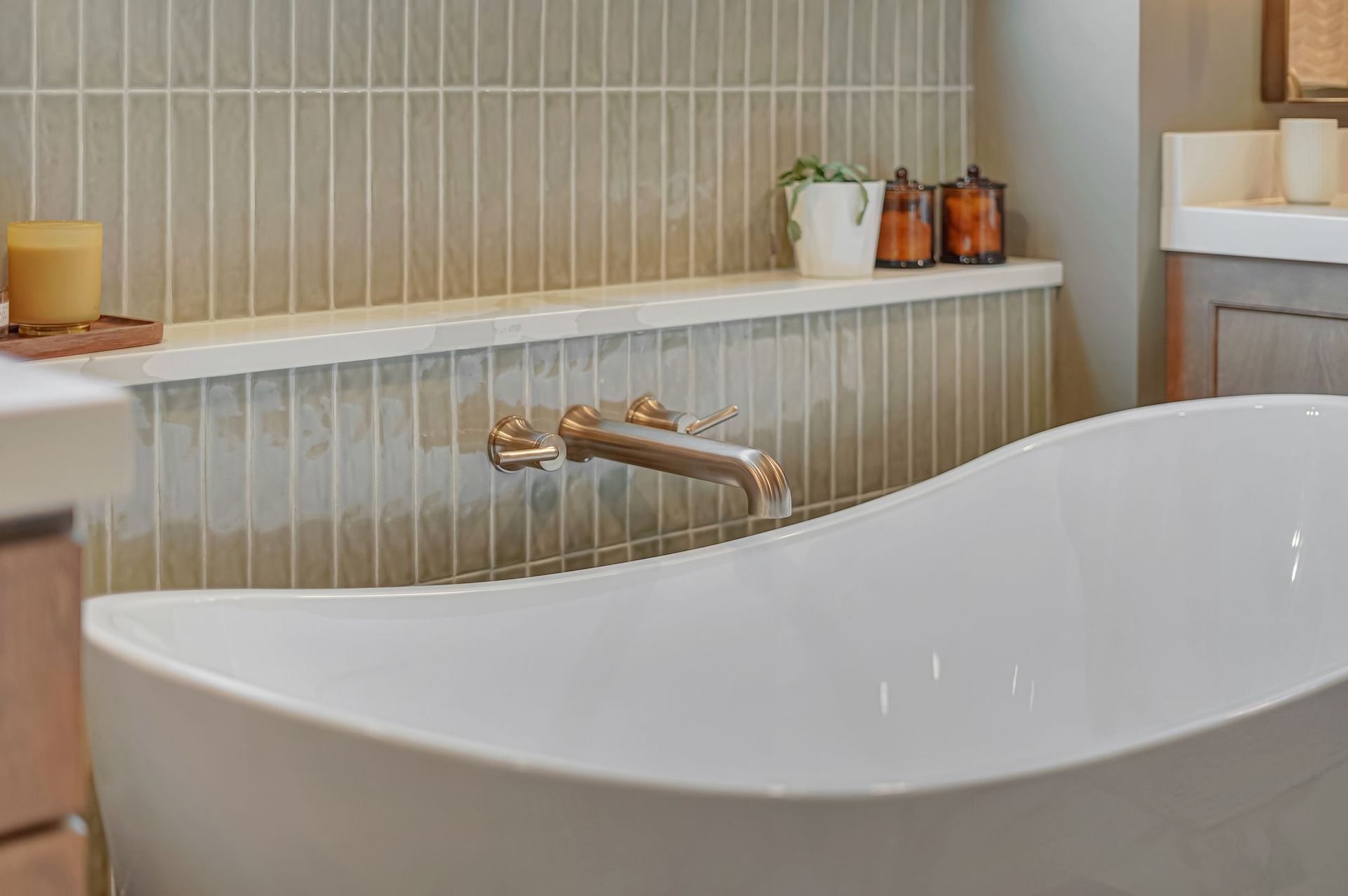 Modern bathroom with white tub, gold faucet, and tan tile wall.
