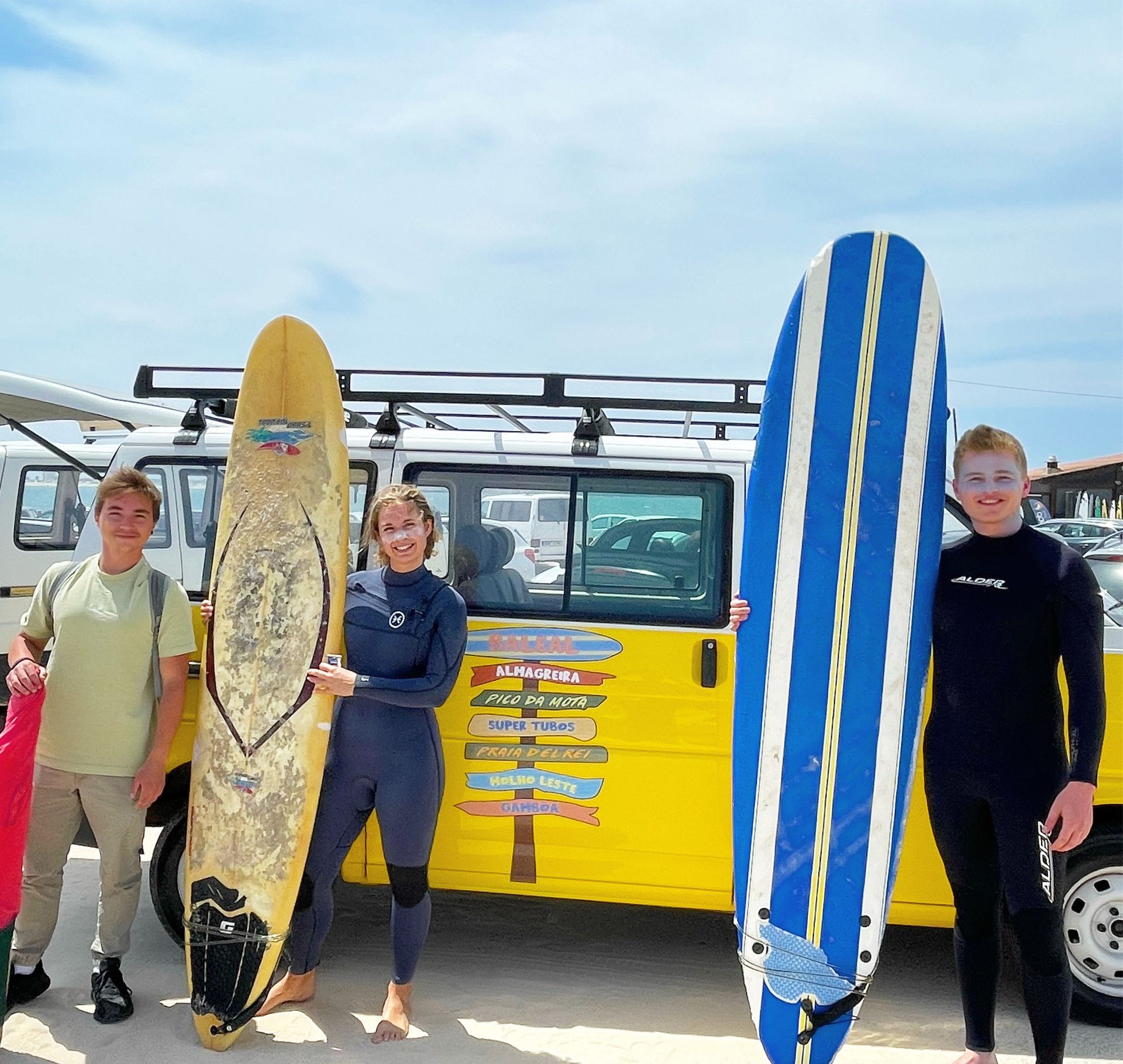 A group of people holding surfboards in front of a yellow van