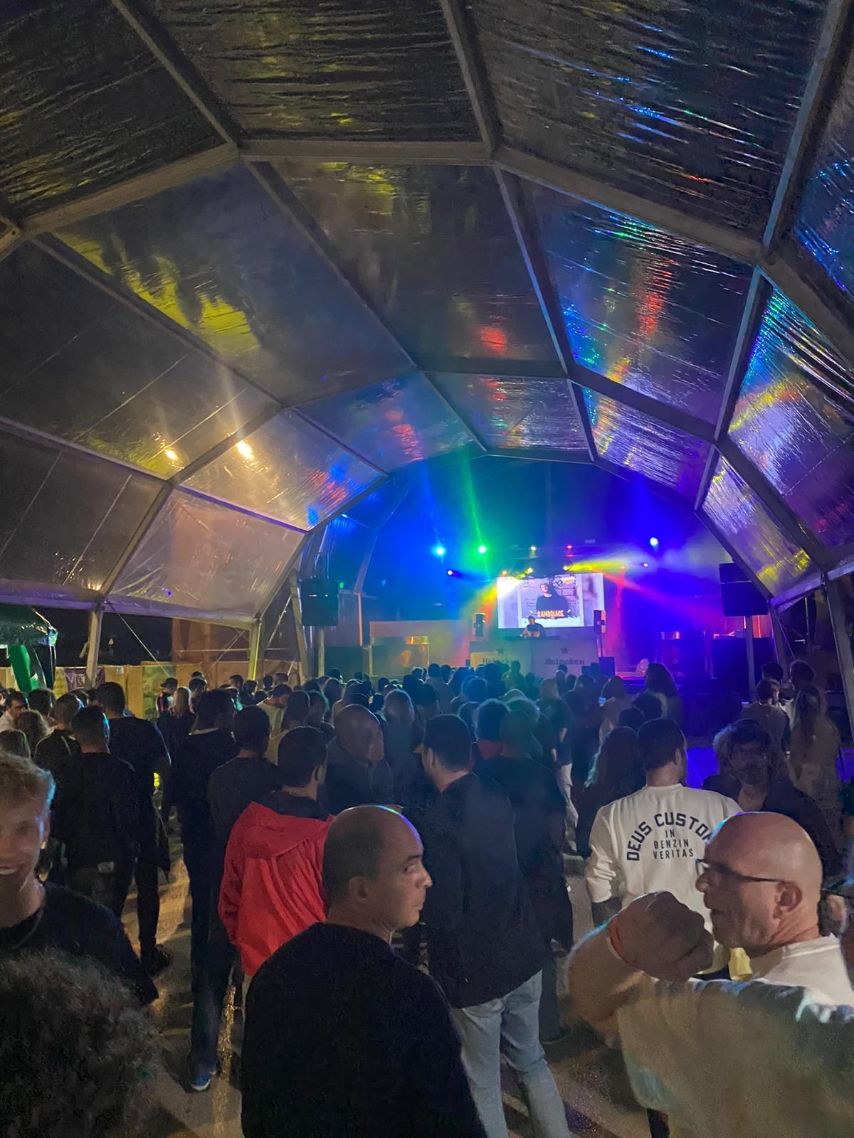 A crowd of people are standing under a clear tent at a concert.
