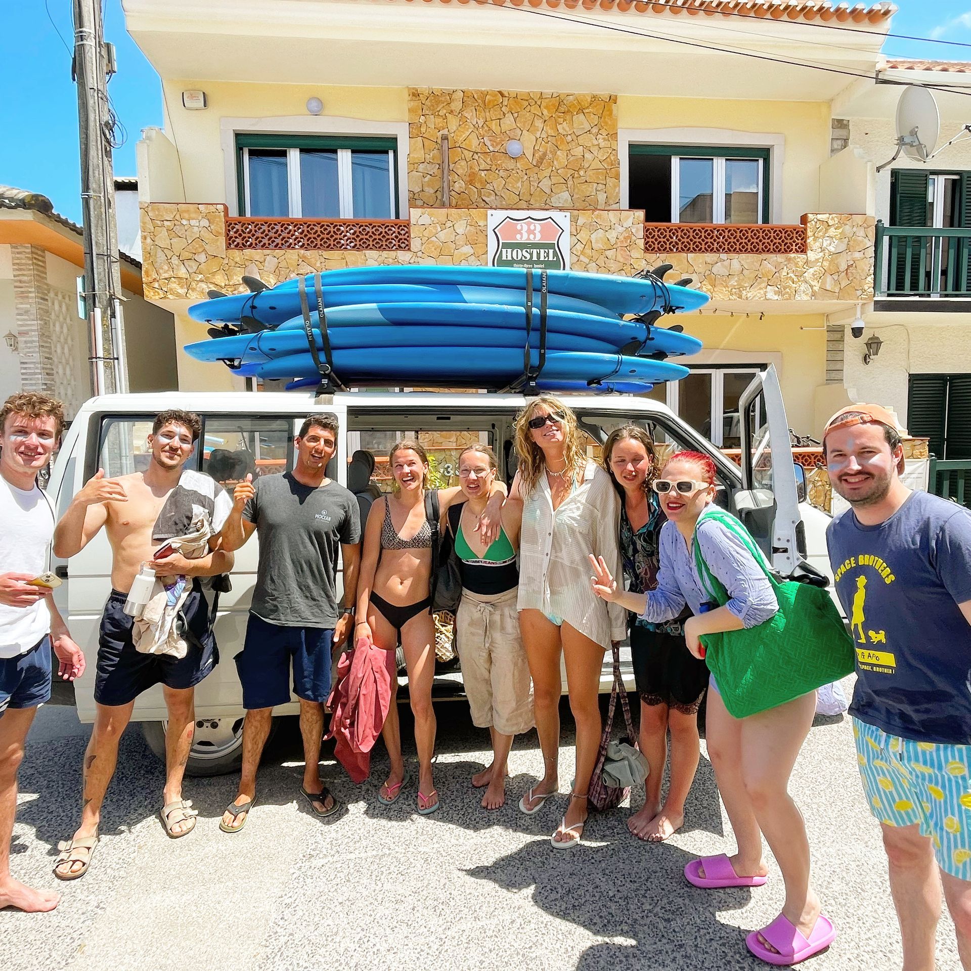 A group of people standing in front of a van with surfboards on top of it