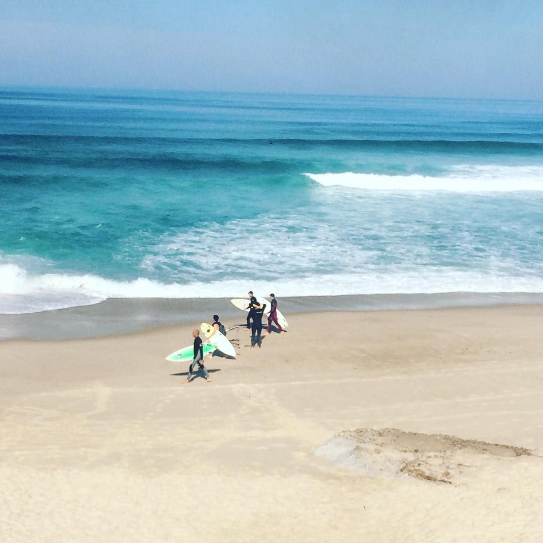 A group of people are walking on a beach carrying surfboards.