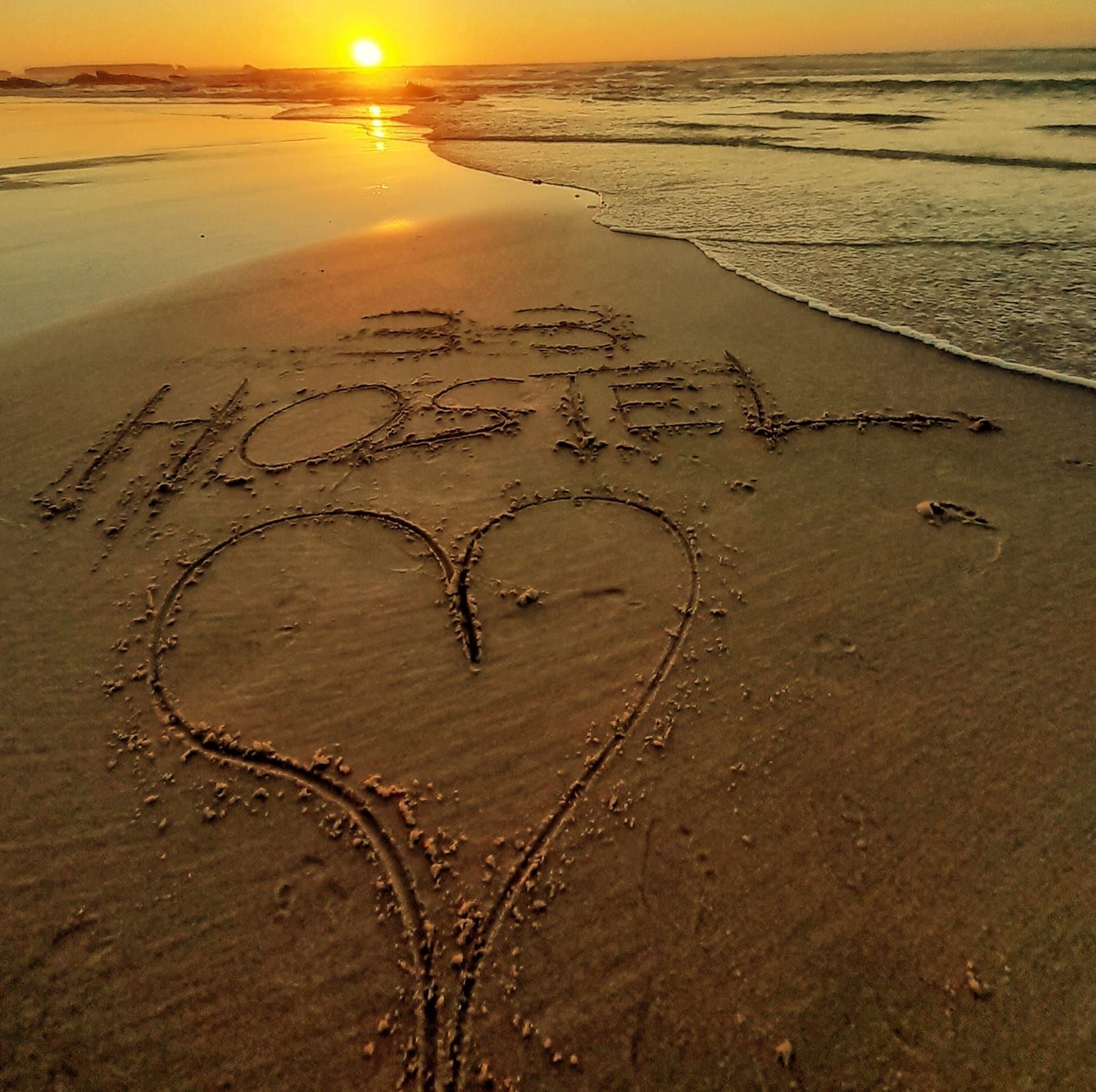 The word hostel is written in the sand on the beach