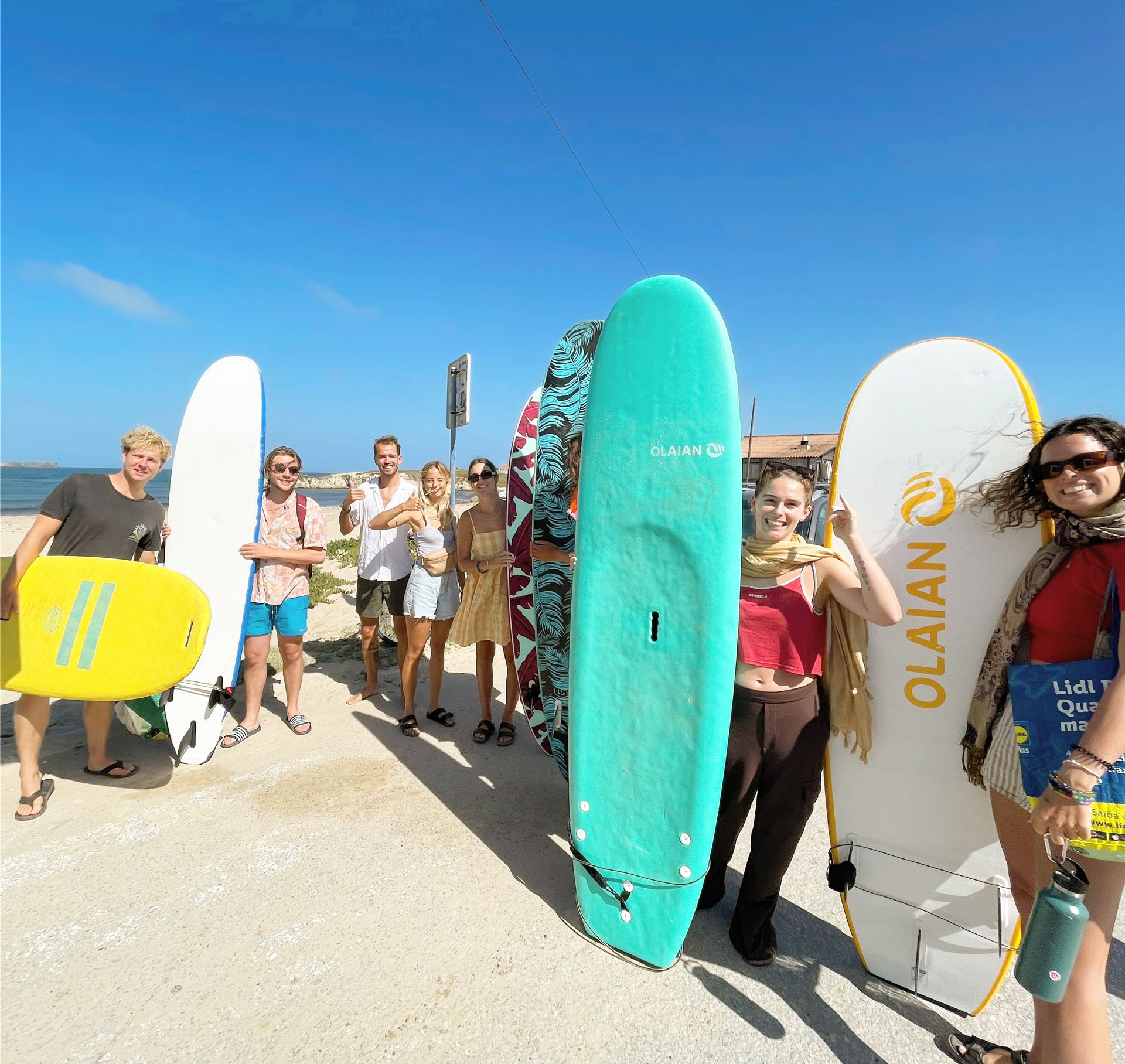A group of people holding surfboards including one that says olaian