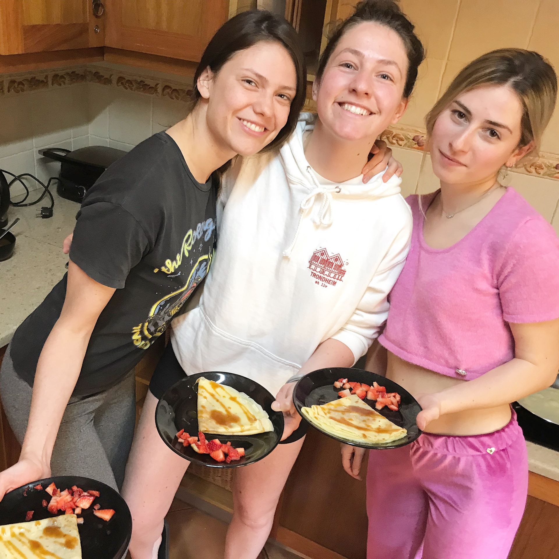 Three women are posing for a picture while holding plates of food