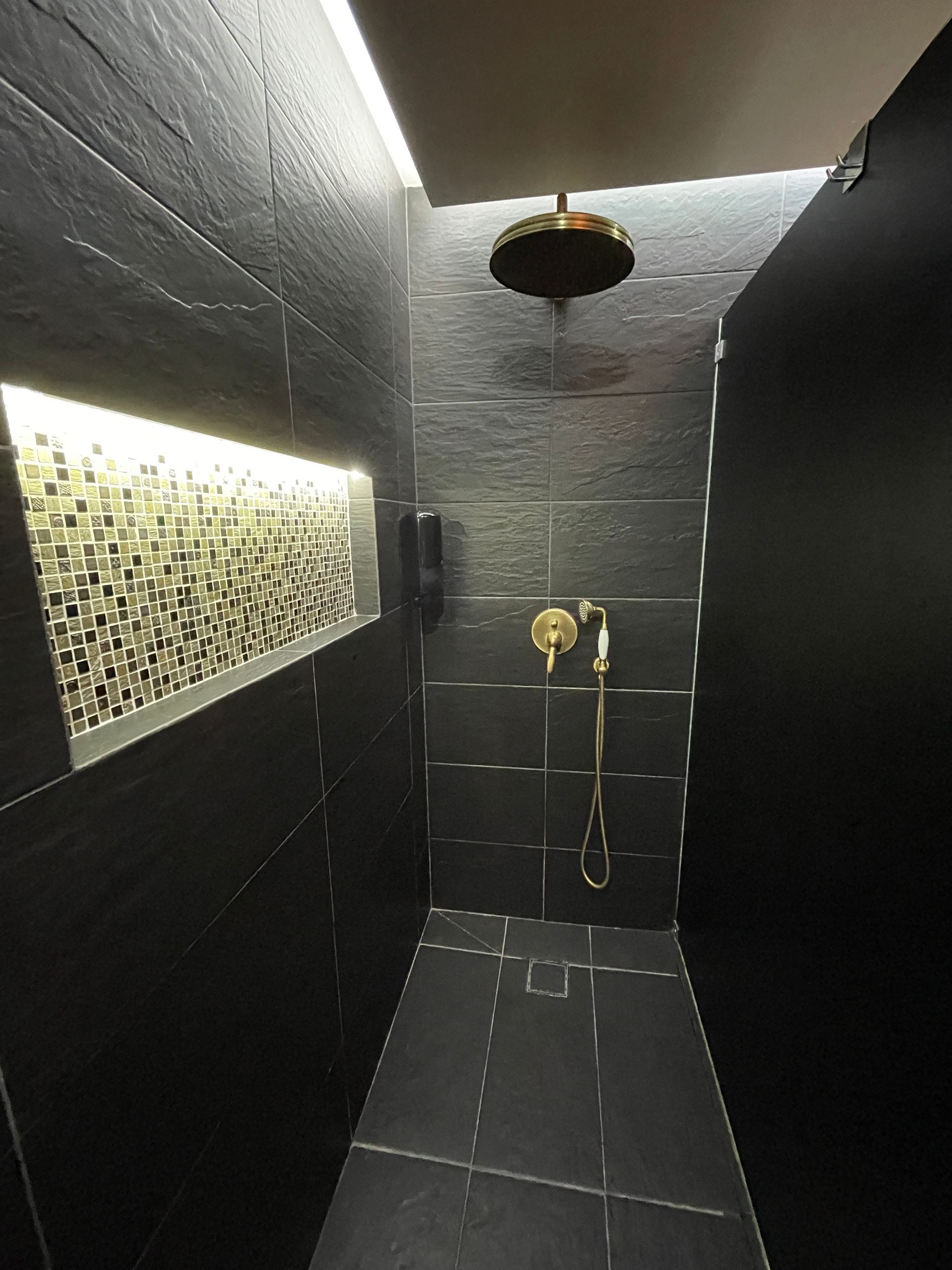 A bathroom with black tiles and a shower head hanging from the ceiling.