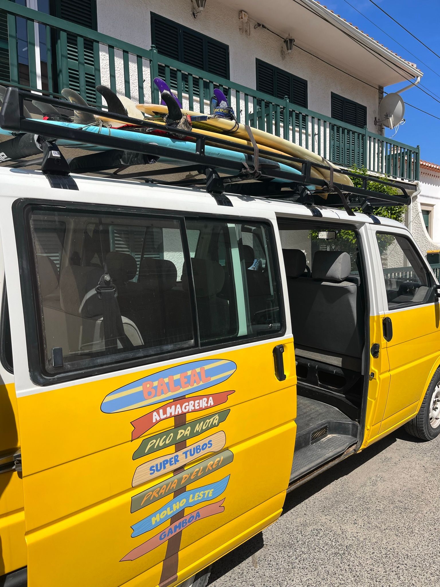 A yellow van with surfboards on top of it is parked in front of a building.