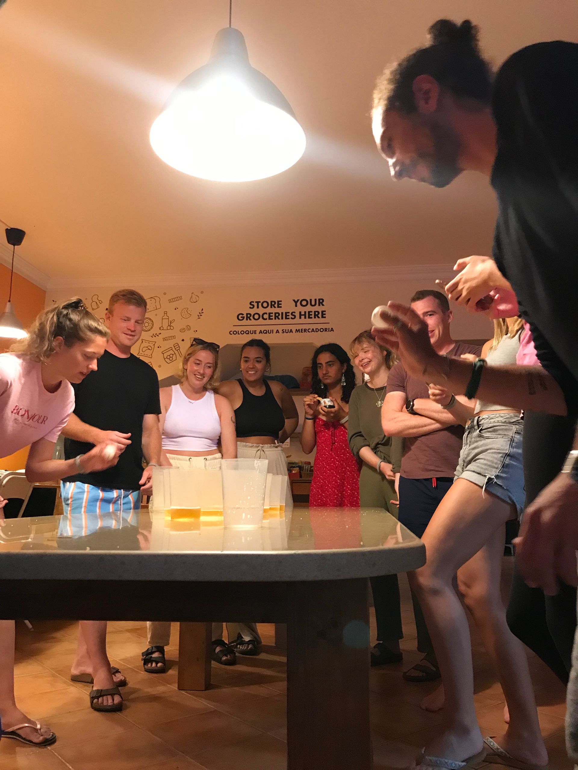 A group of people are standing around a table playing beer pong
