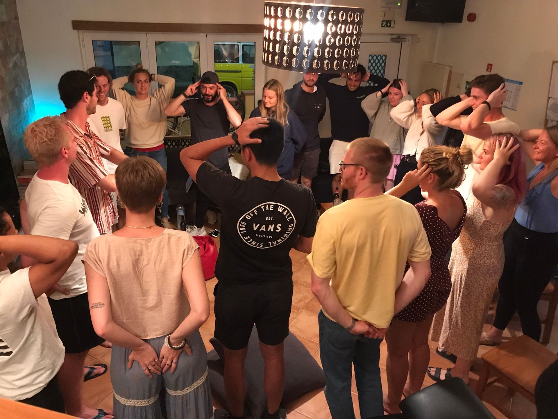 A group of people are standing in a circle with their hands on their heads.