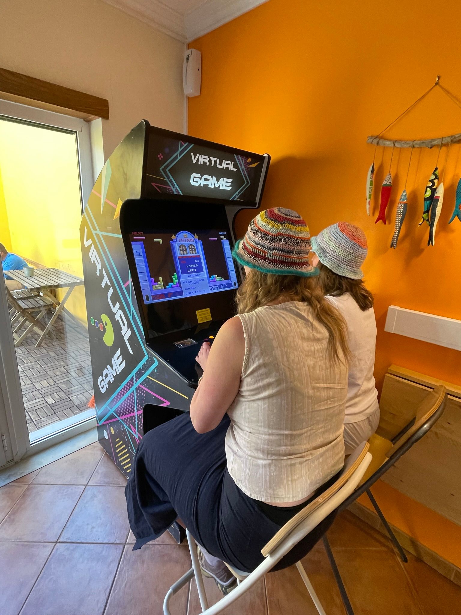 Two women are sitting in chairs playing an arcade game.