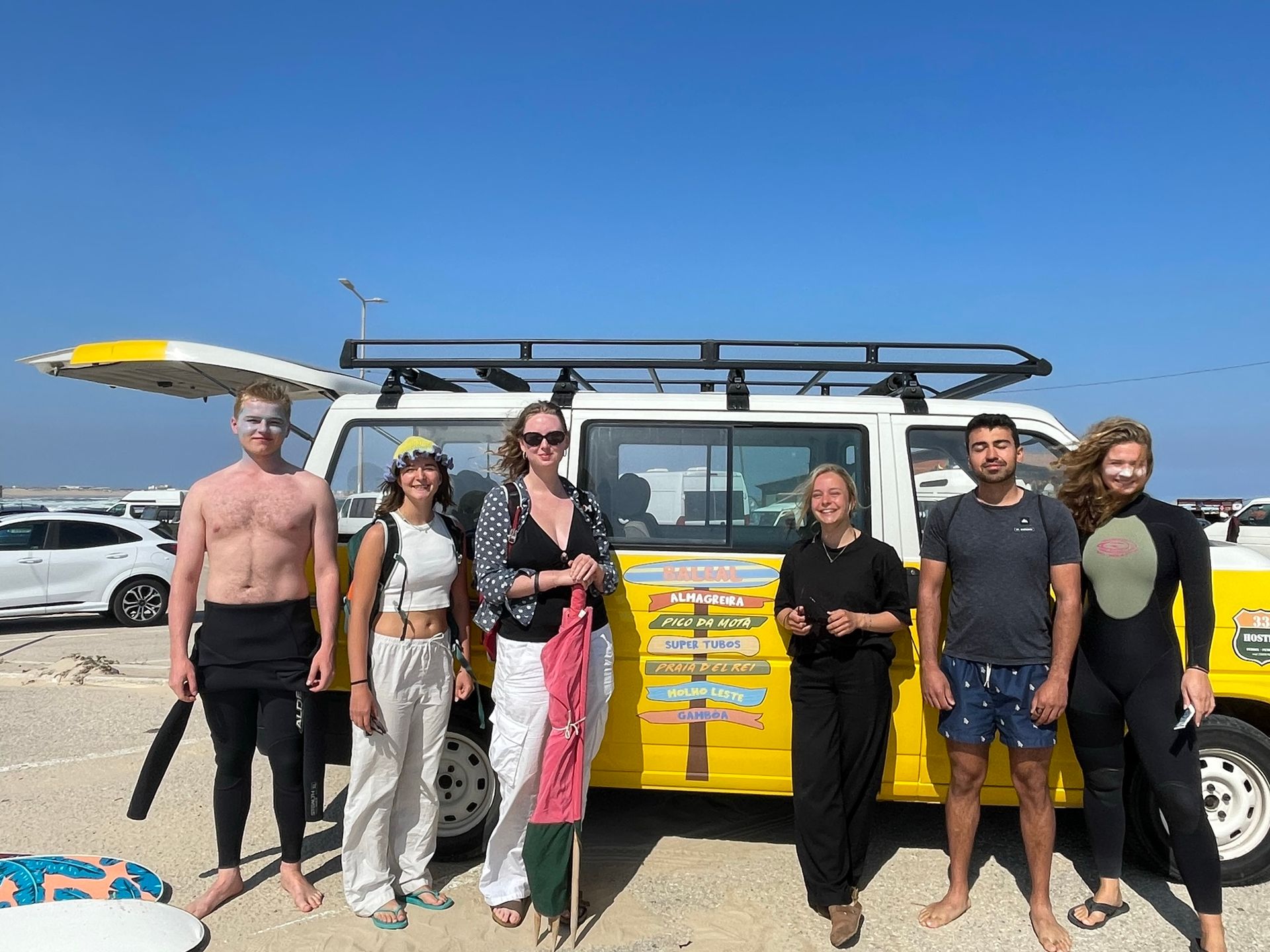 A group of people standing in front of a yellow van on the beach.