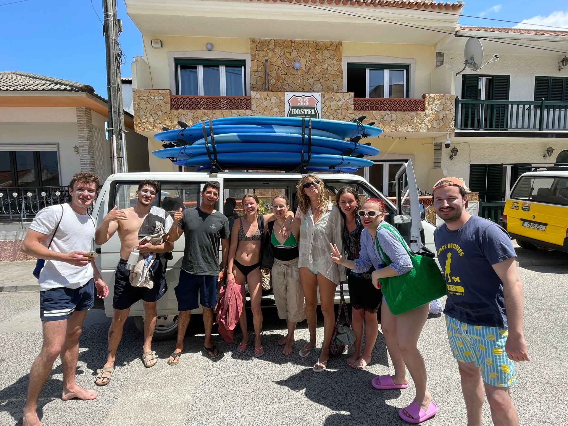 A group of people standing in front of a van with surfboards on top of it.