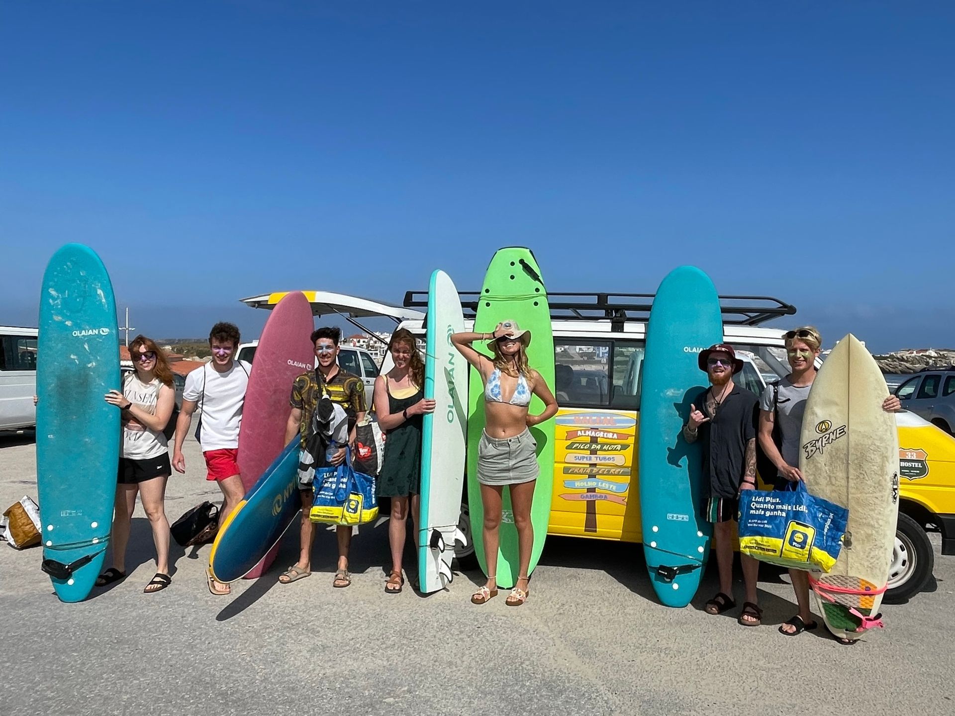 A group of people holding surfboards in front of a yellow van