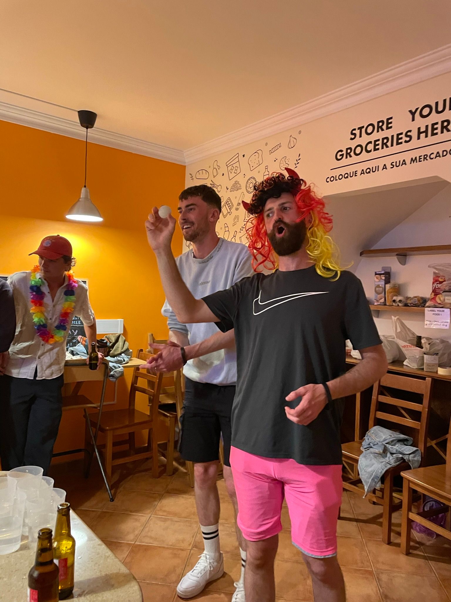 A group of men are standing in a room and one of them is wearing a wig.