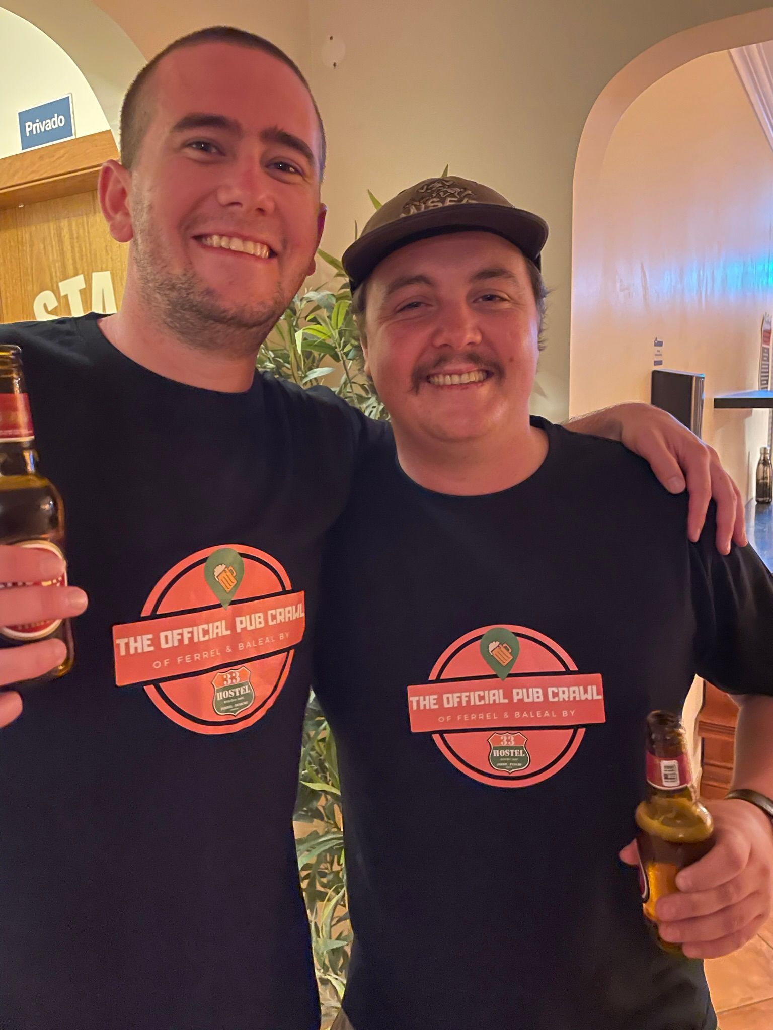 Two men are posing for a picture and one of them is holding a bottle of beer.