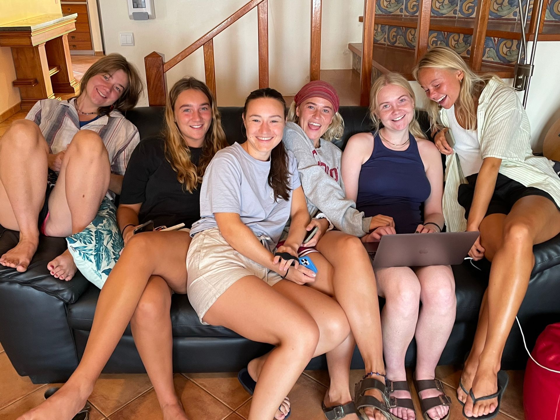 A group of young women are sitting on a couch with laptops.
