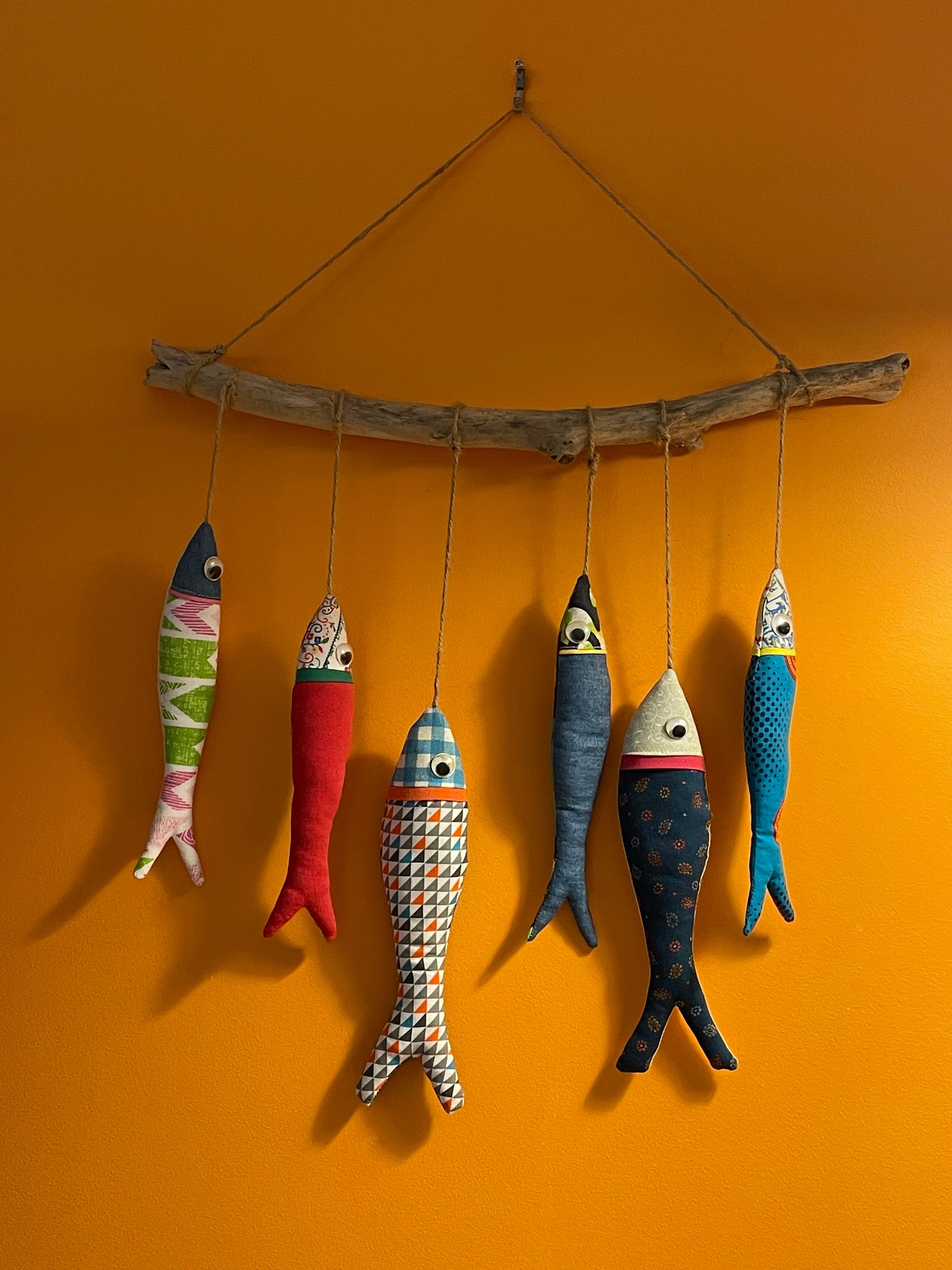 A bunch of stuffed fish hanging from a string on an orange wall