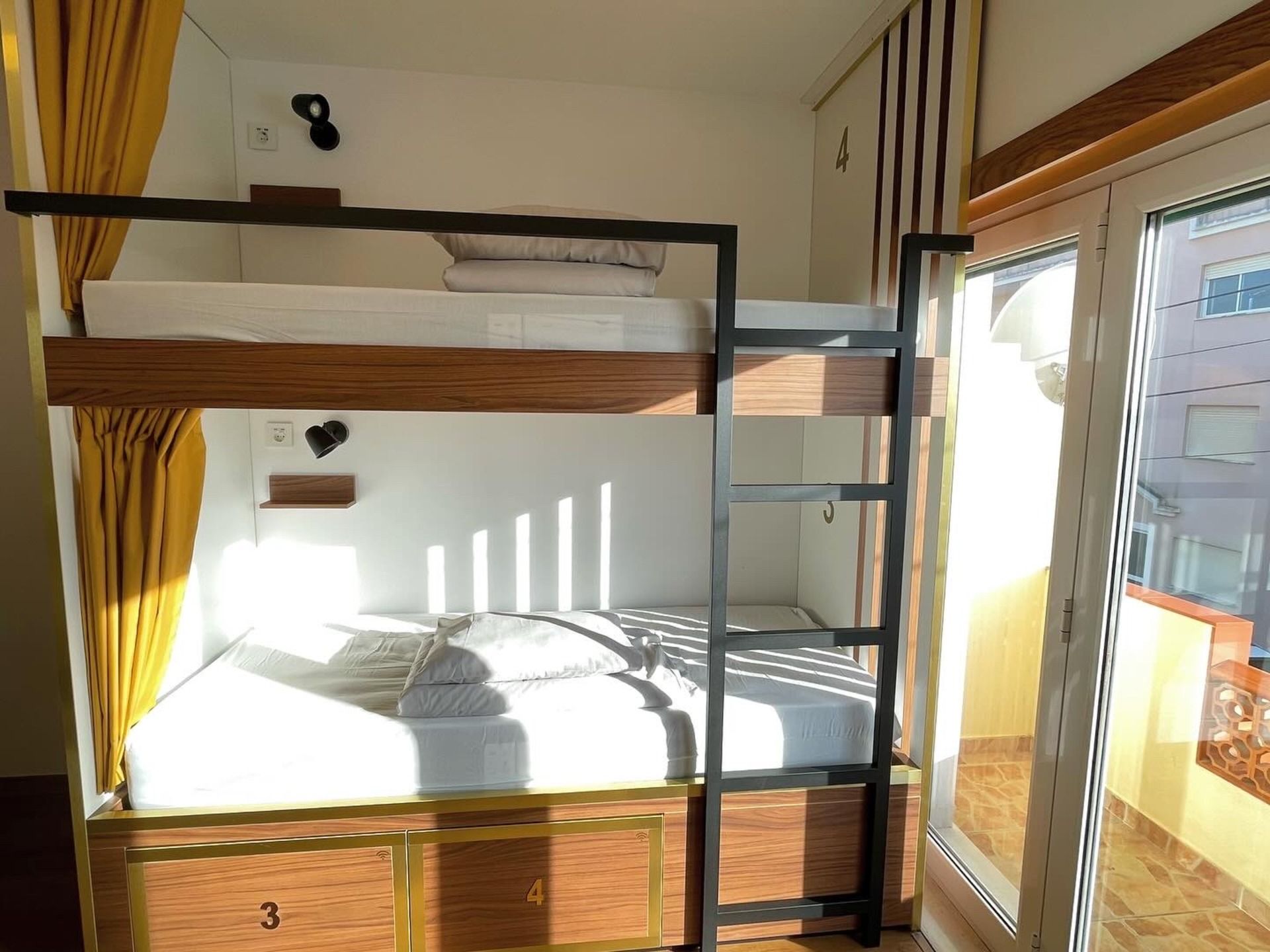 A bunk bed with a ladder in a room next to a window.