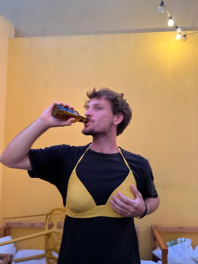 A man wearing a bikini top is drinking from a bottle