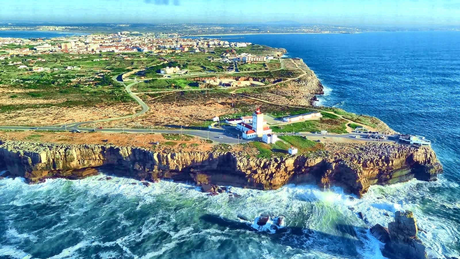 An aerial view of a lighthouse on a cliff overlooking the ocean.