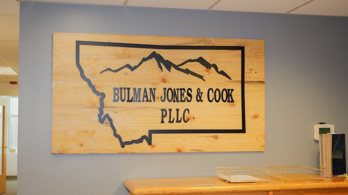 Sign for Bulman Jones & Cook PLLC on a wooden board featuring a Montana outline with mountains and text.