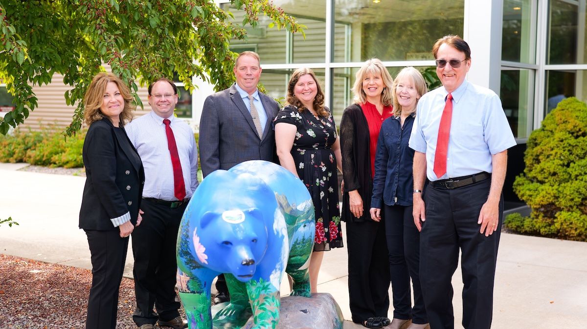 Group of people posing by a painted bear statue outside a building.