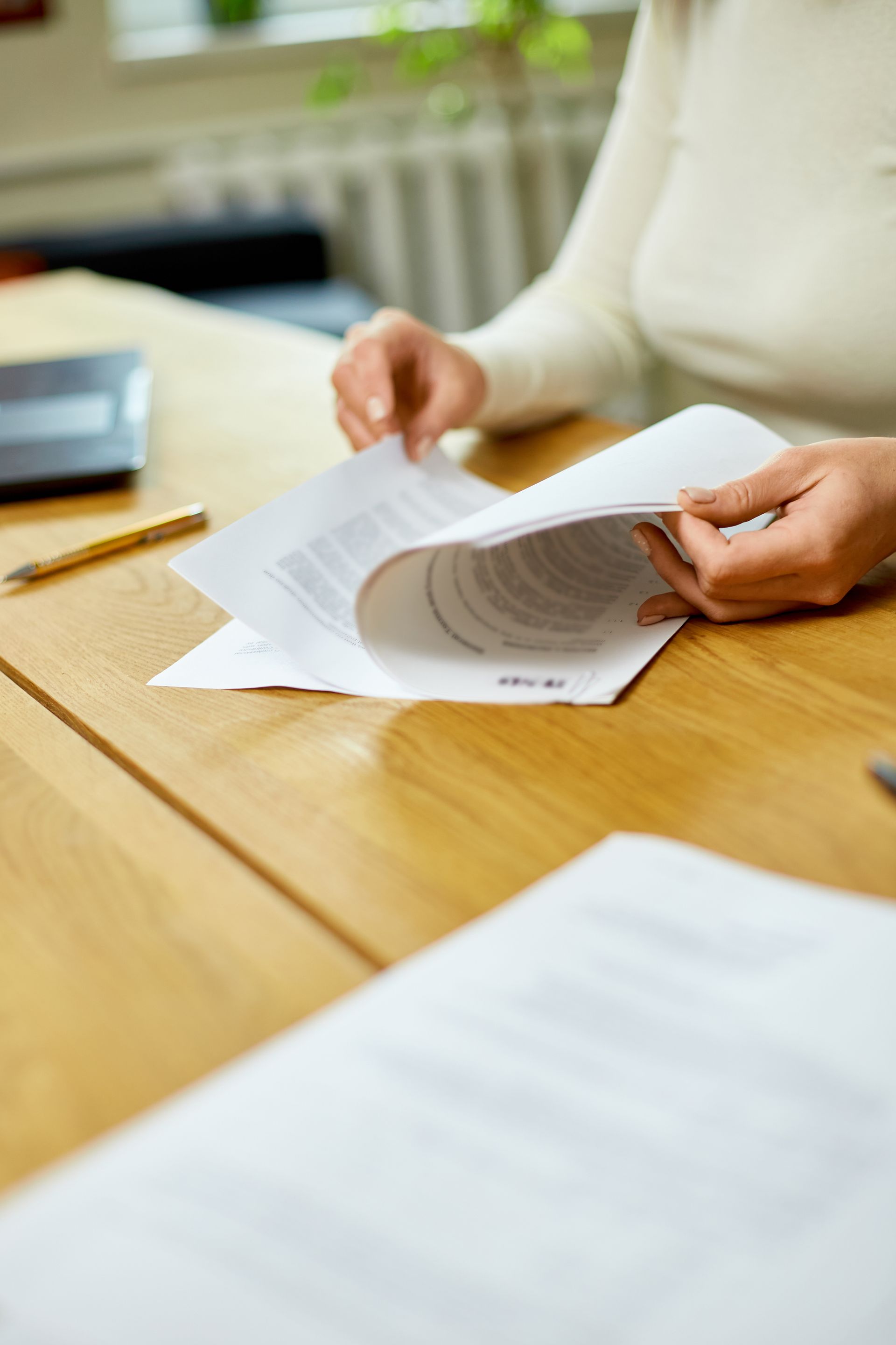 Person turning pages of paperwork at a wooden table. A pen and laptop are nearby.