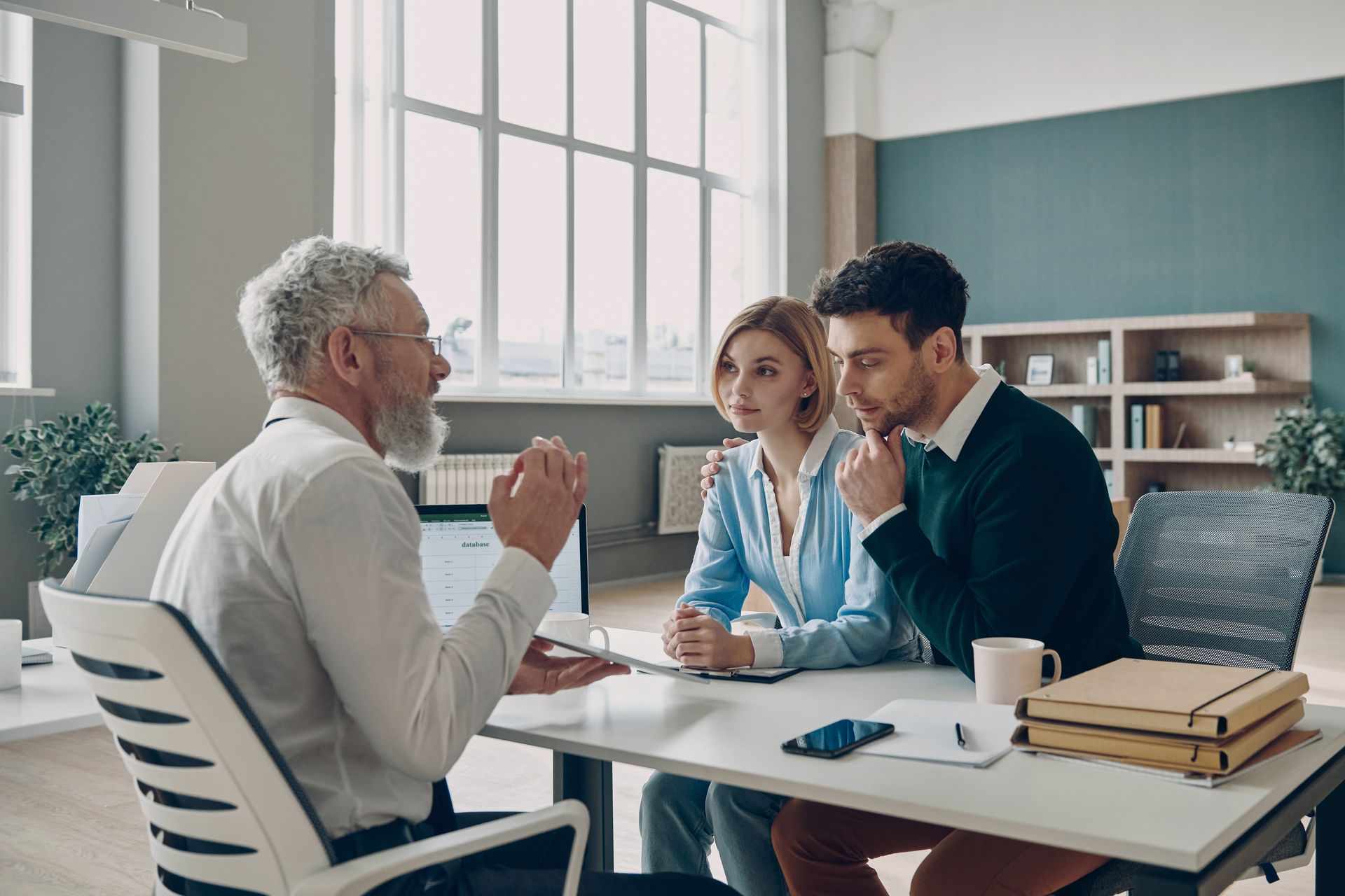 Man talking to a couple at a desk. The couple listens intently. Modern office setting.
