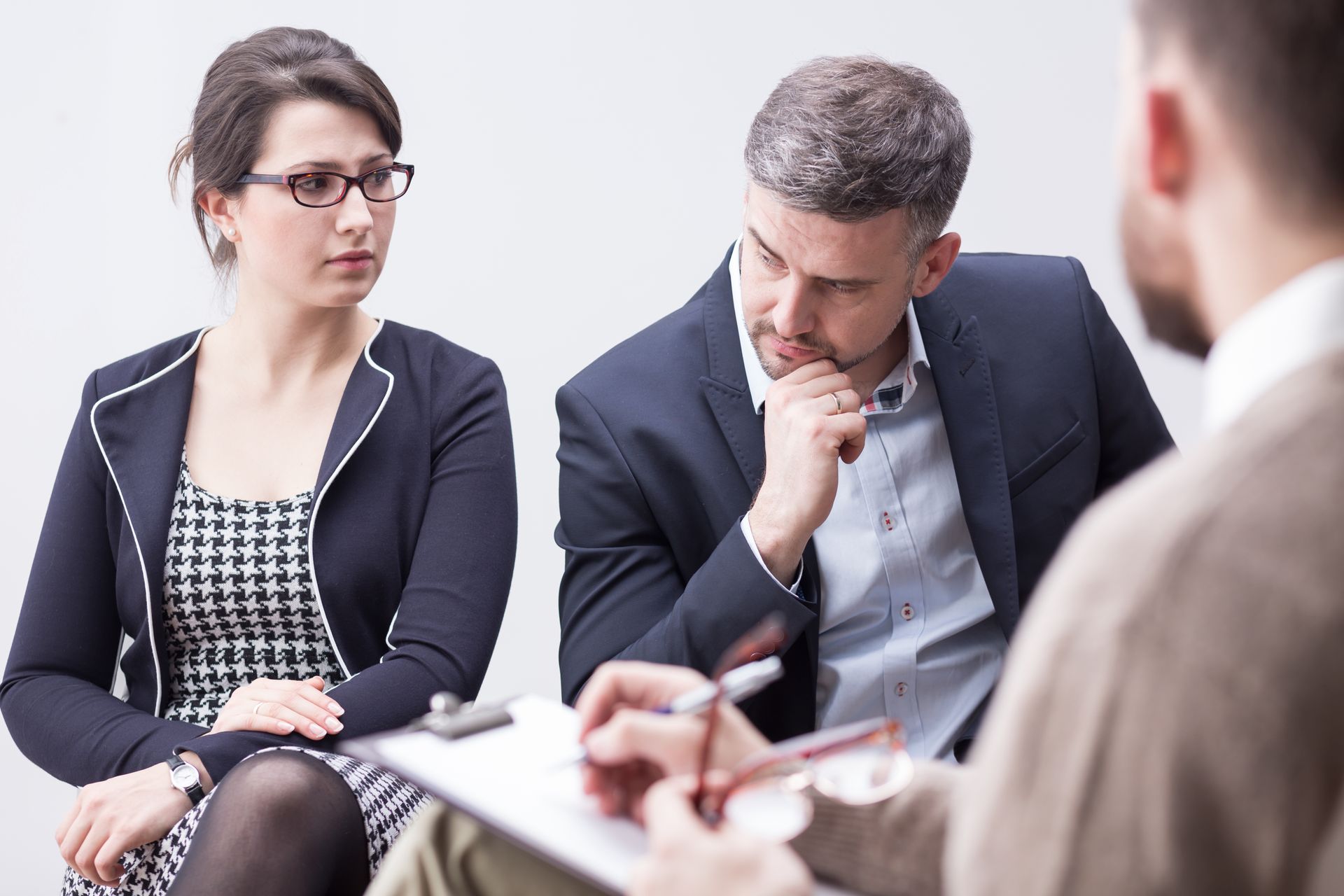Couple in therapy session, listening to therapist taking notes.