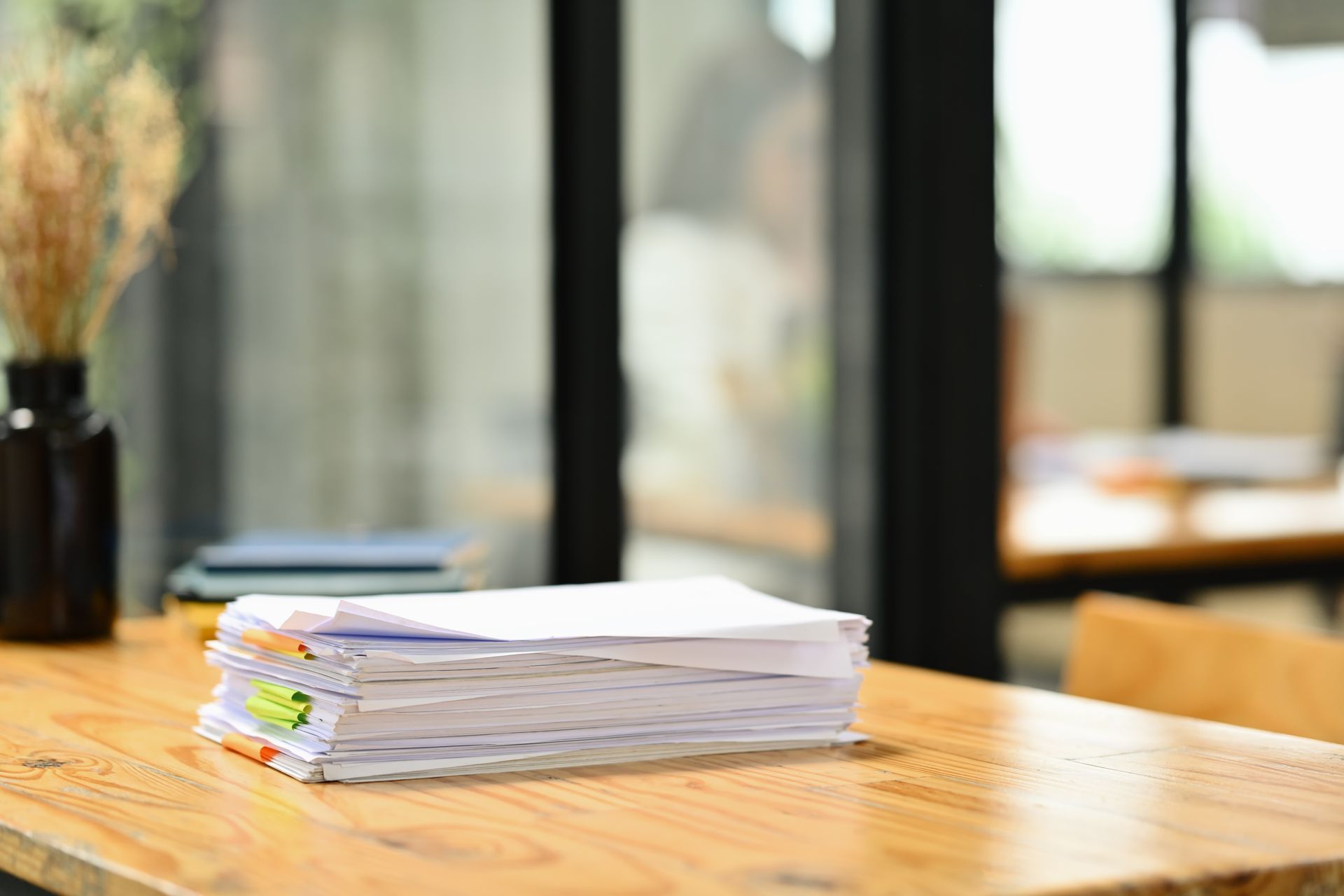 Stack of papers on a wooden table with a blurred background of a room.