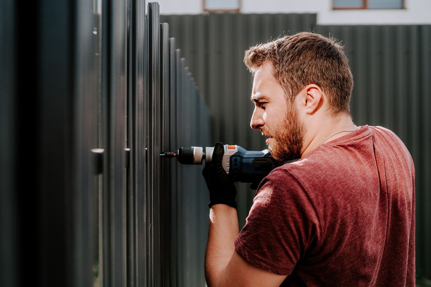 Technician fastening fence hardware using an electric screwdriver.