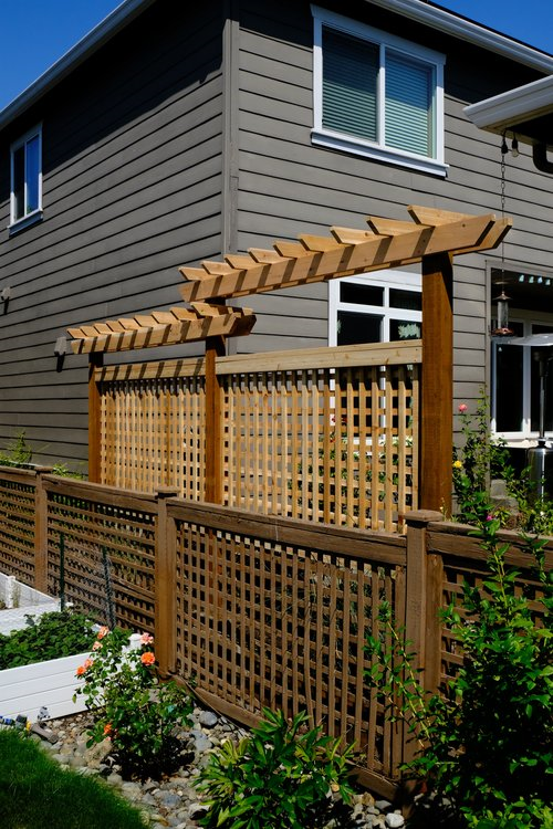 Wooden lattice fence with a pergola-like top section, set against a gray house exterior.