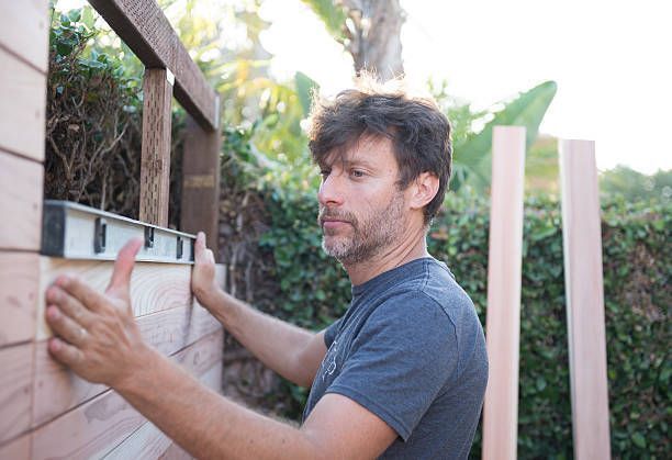 Man installing wooden fence panel using a level tool outdoors