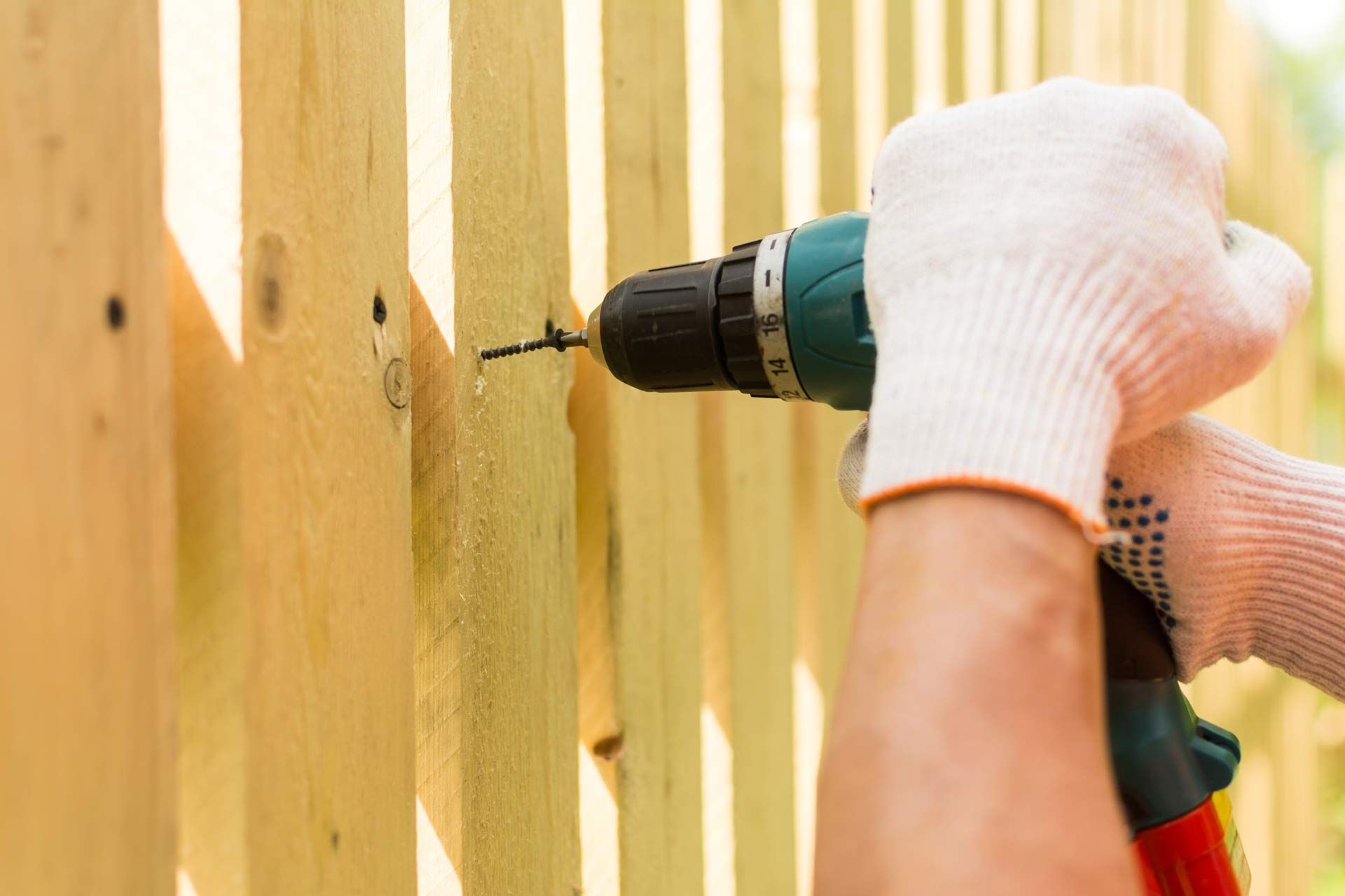 Fence installation contractor’s hands, holding an electric screwdriver for wood fence installation.