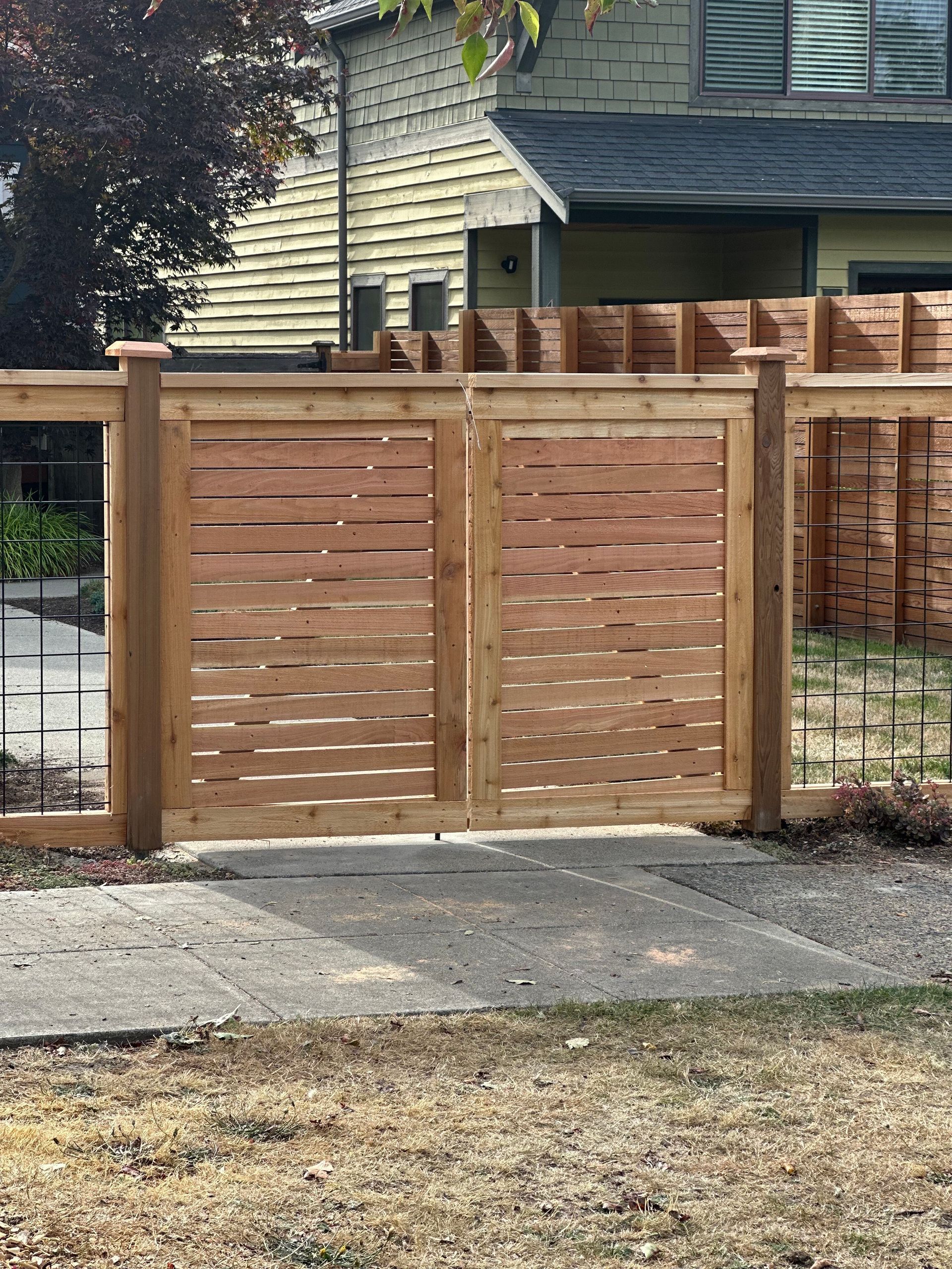 Wooden double gate with horizontal slats, on a concrete driveway, in front of a house.