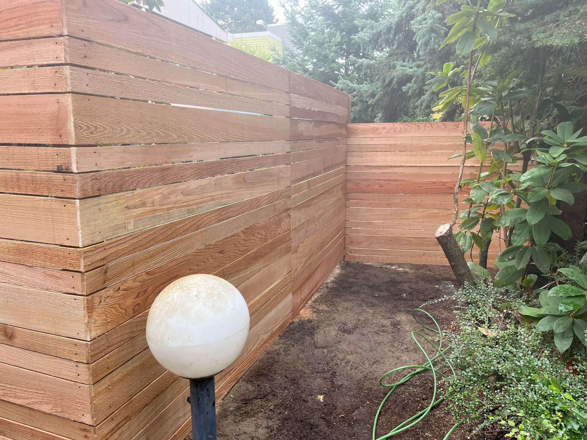 Wooden fence in a yard with a globe light post and greenery.
