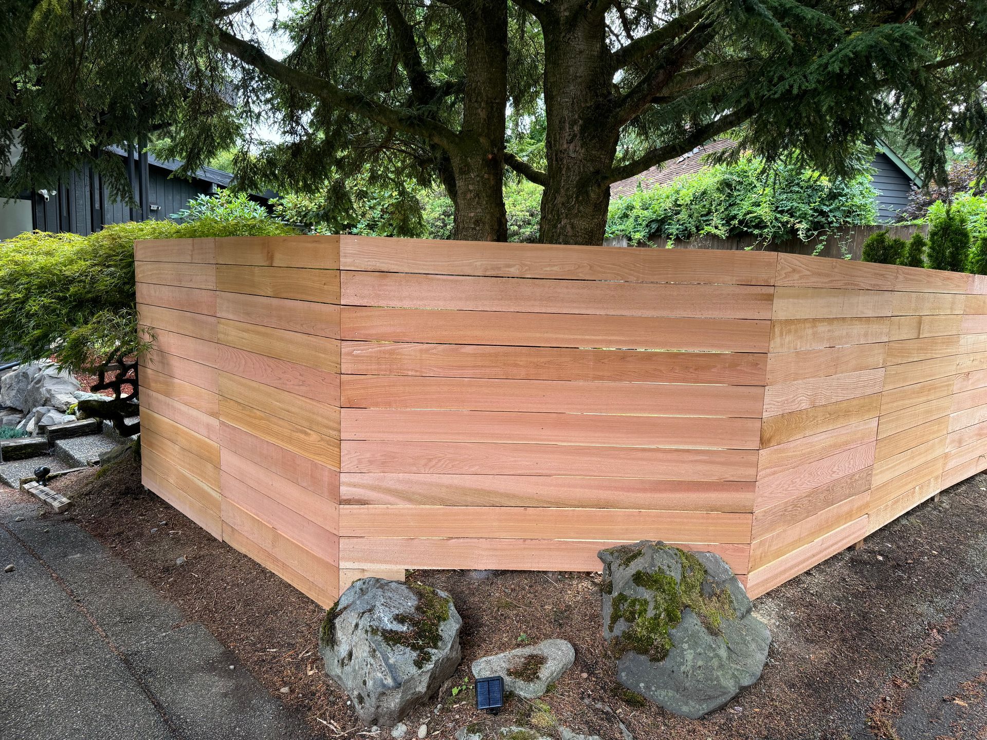 A wooden fence is surrounded by snow in front of a house.