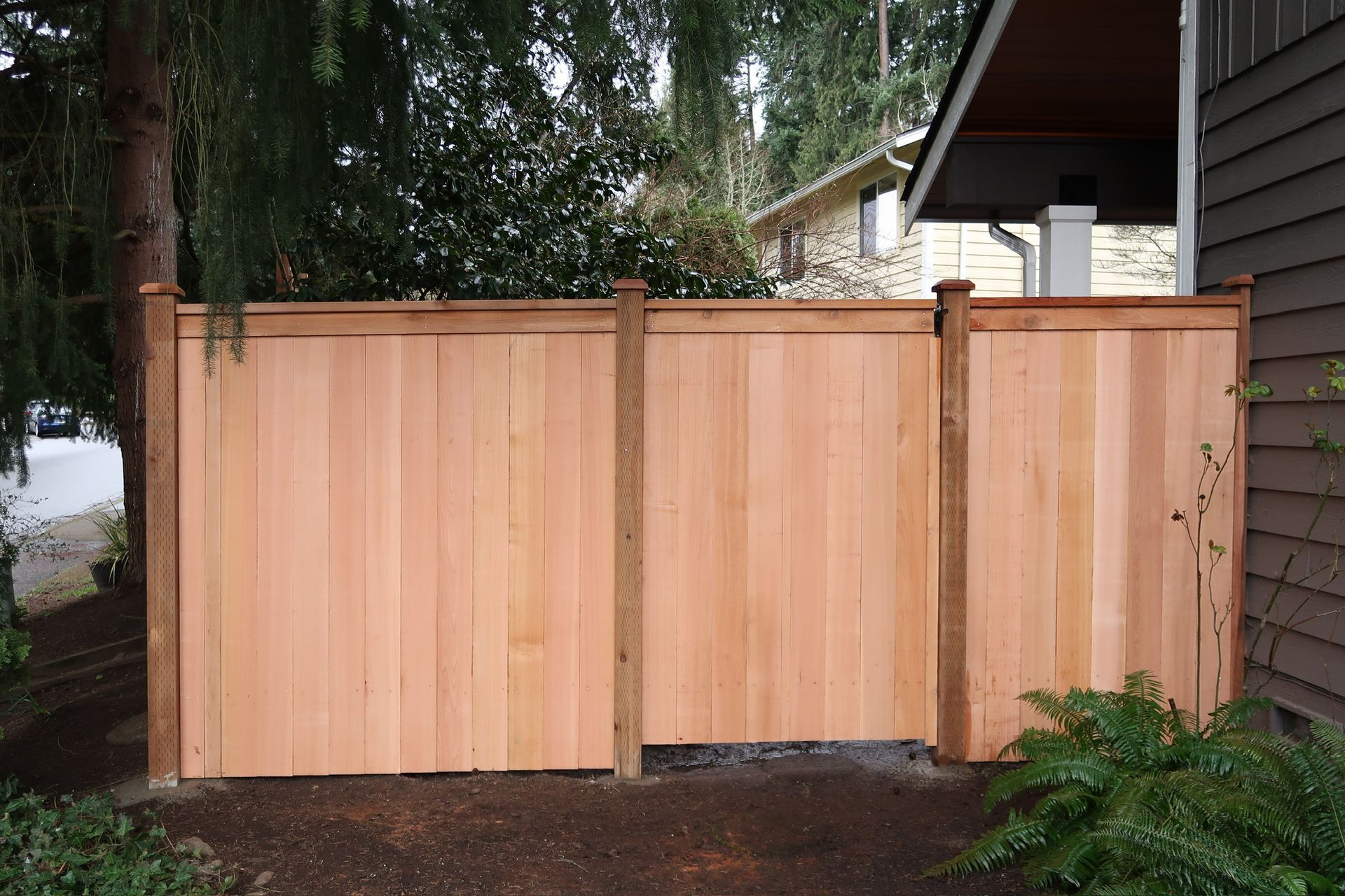 There is a wooden fence in the backyard with a lot of leaves on the ground.