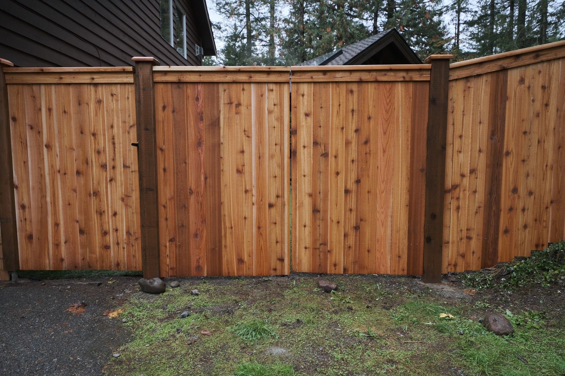 Wooden privacy fence with gate in front of a house, set in grass.