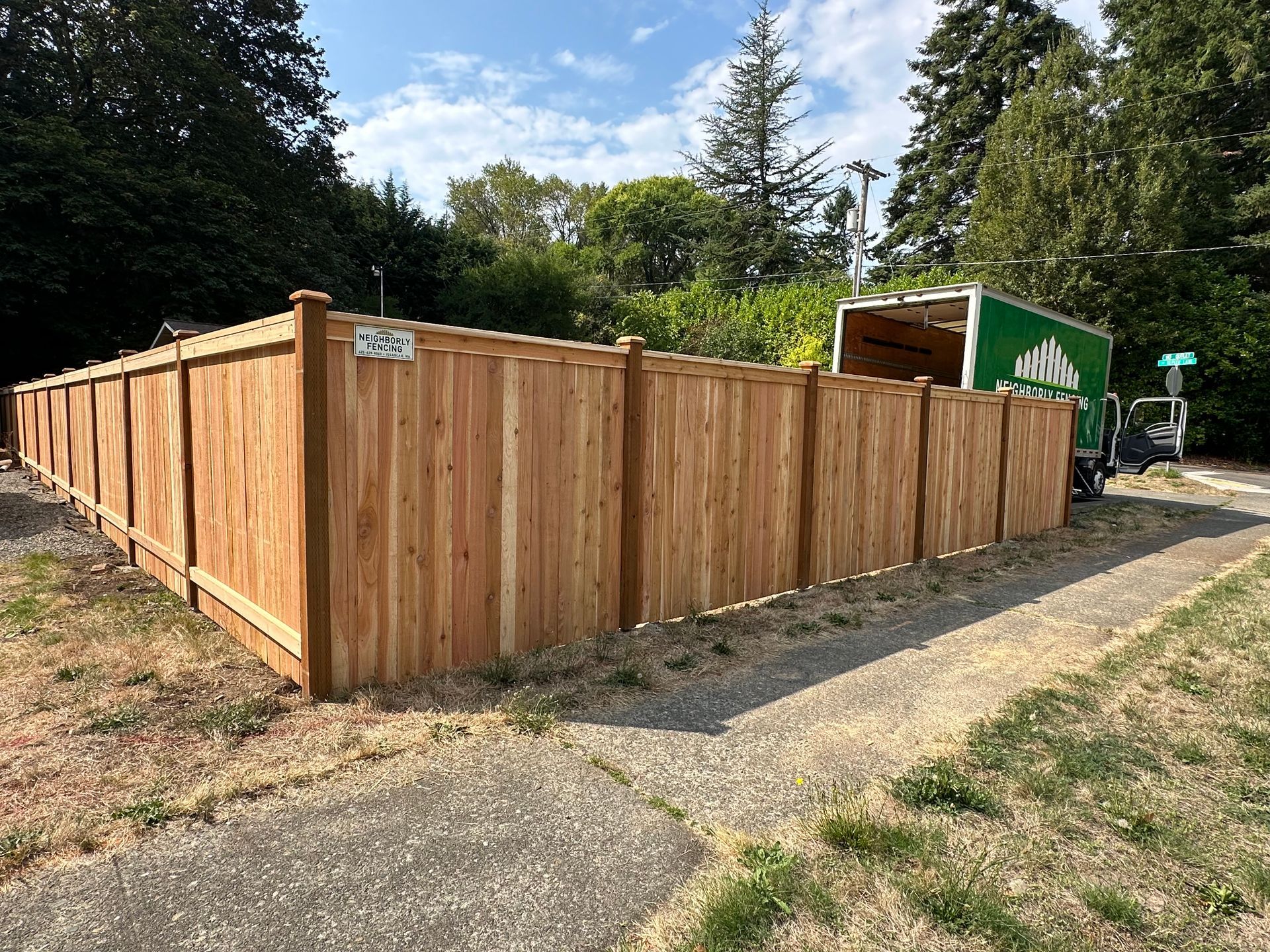 Wooden fence alongside a sidewalk, with a green truck in the background.