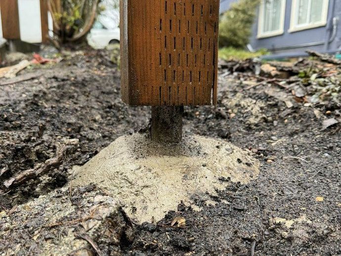 Wooden post set in concrete in muddy ground.
